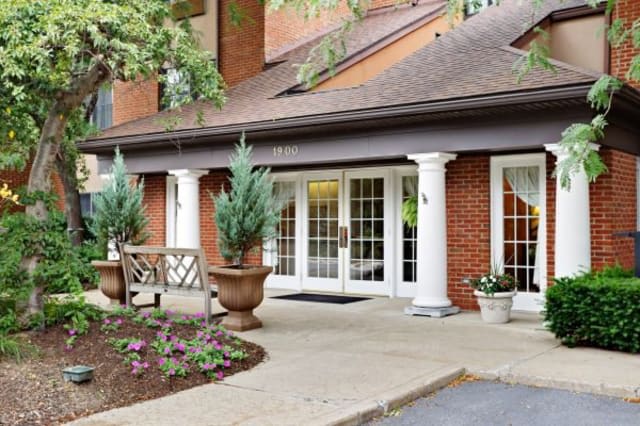 A welcoming building entrance with brick facade and white columns, surrounded by potted plants.