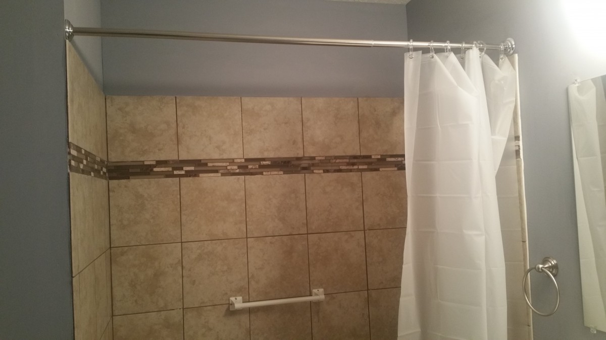 A bathroom with a tiled wall and a shower curtain hanging from a rod.
