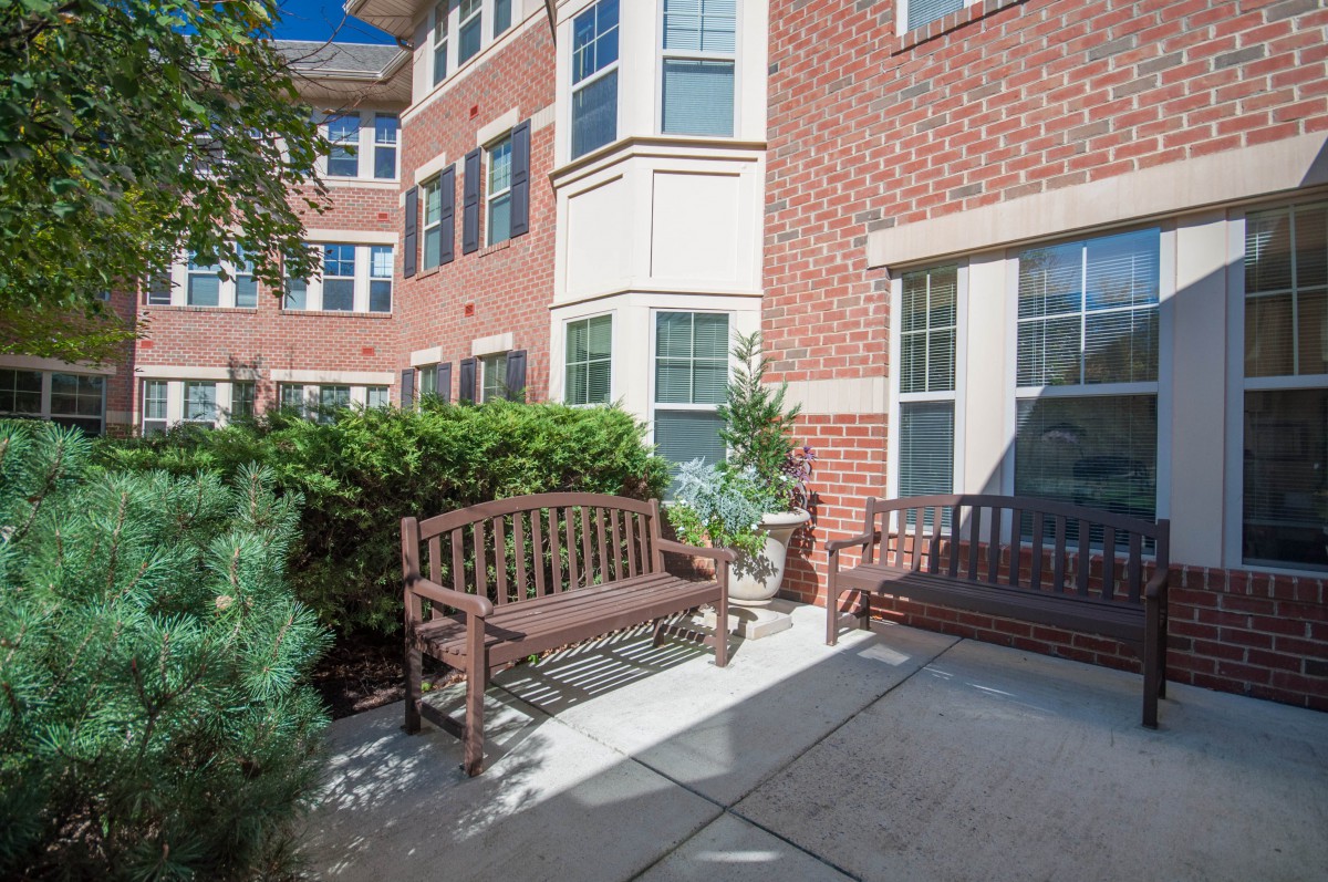 A cozy patio area with wooden benches in front of a brick residential building.