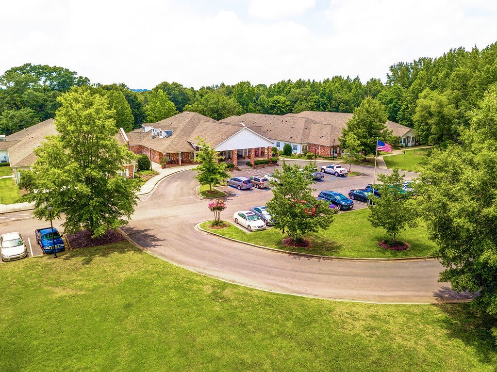 Aerial view of a large building surrounded by trees and a parking lot filled with cars.