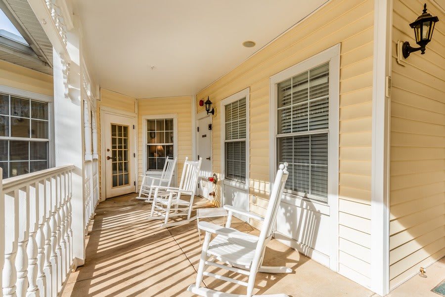 A sunny front porch with white rocking chairs and yellow siding.