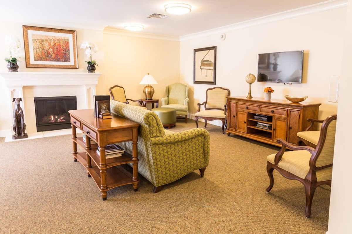 A cozy living room with classic furniture, including a sofa and armchairs around a coffee table, a fireplace, and a TV stand.