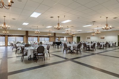 An empty banquet hall with elegantly set tables, chandeliers, and a grand piano.