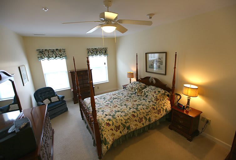 A cozy bedroom featuring a bed with floral bedding, two bedside lamps, and a ceiling fan.