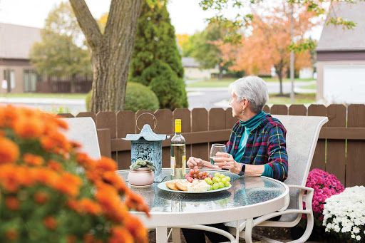 An elderly woman enjoys a serene moment outdoors, sipping wine and savoring snacks amidst the autumn scenery.