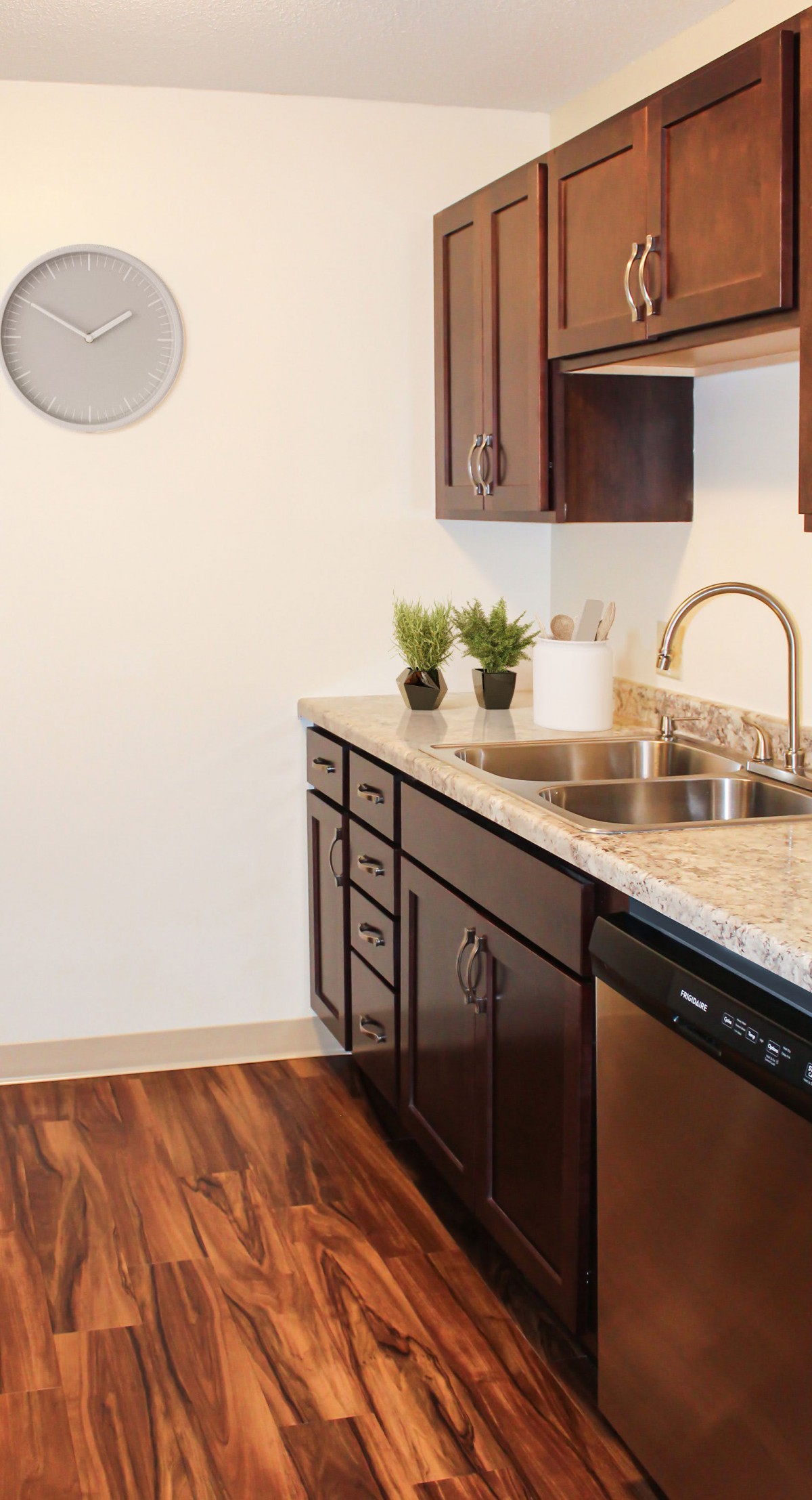 A modern kitchen with a double sink, wooden cabinets, and decorative plants on the countertop.