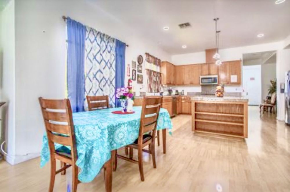 A modern kitchen and dining area with wooden furniture, blue curtains, and a turquoise tablecloth.