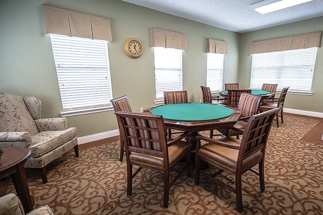 A carpeted room with multiple poker tables and chairs arranged near several windows.