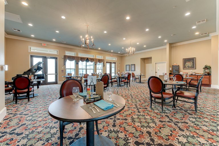 A spacious and elegantly decorated dining room with several tables and chairs, adorned with chandeliers and a patterned carpet.