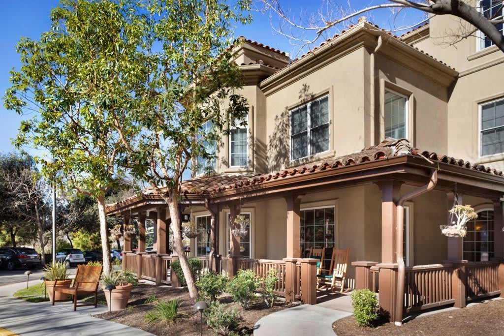 A beautiful two-story stucco house with a terracotta roof, surrounded by lush greenery on a sunny day.