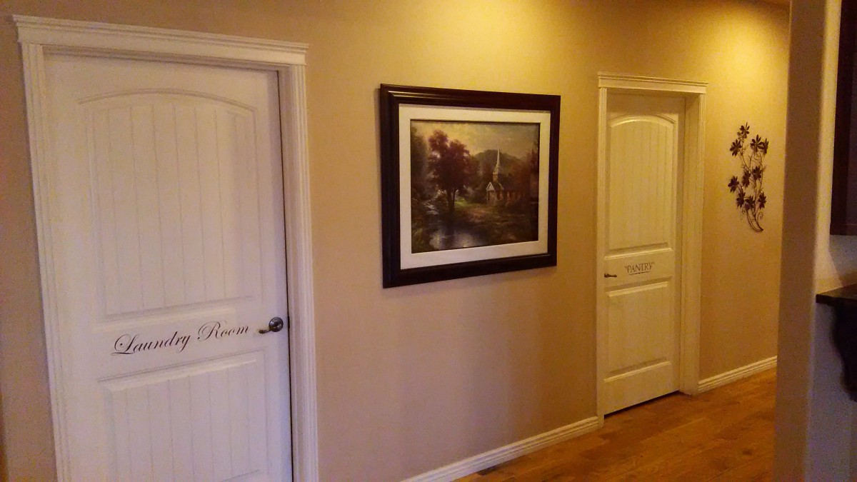 A hallway featuring a framed landscape painting on the wall with two white doors on either side.