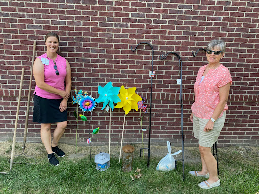 Two individuals pose beside colorful garden decorations in an outdoor setting.