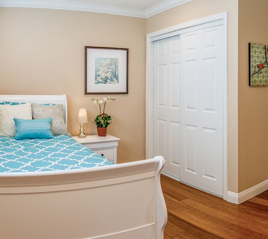 A cozy bedroom featuring a bed with a blue patterned cover, a nightstand with a lamp and plant, and a closed closet with sliding doors.
