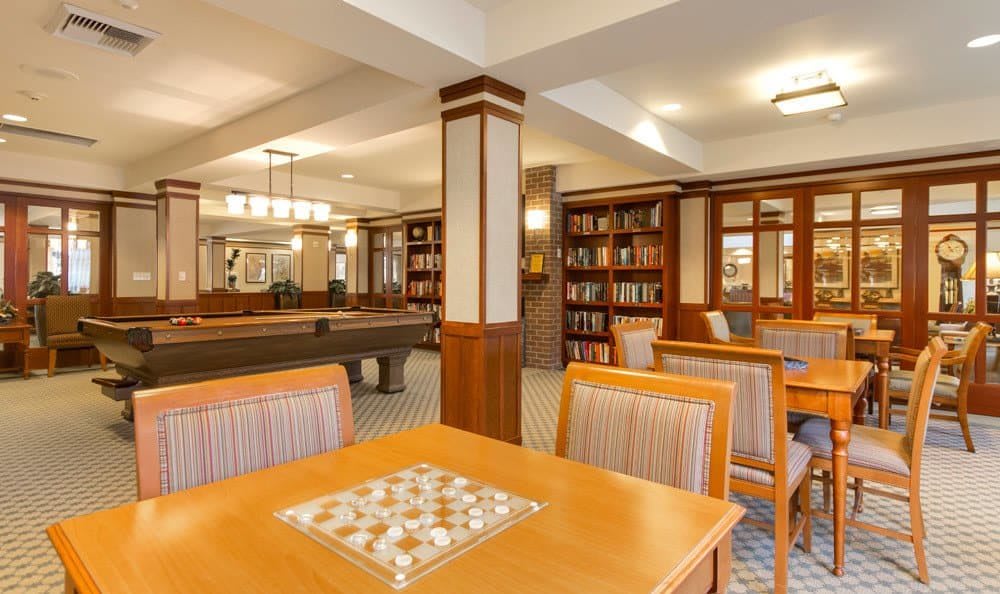 A cozy library with wood furniture, bookshelves, and a pool table.