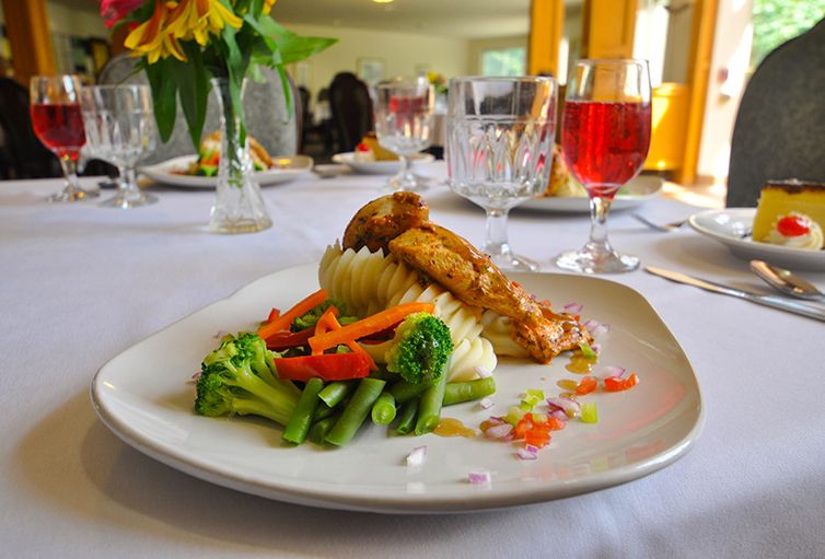 A beautifully plated gourmet meal featuring chicken and mixed vegetables, accompanied by a glass of wine on an elegantly set table.