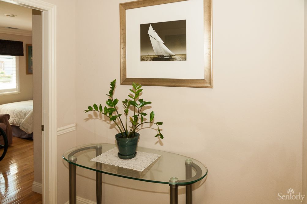 A glass table with a potted plant beneath a framed picture in a hallway.
