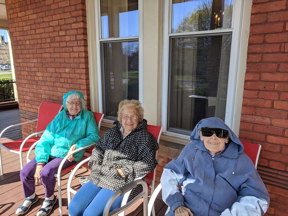 Three elderly women sitting on a porch, bundled up in coats, enjoying the outdoors.