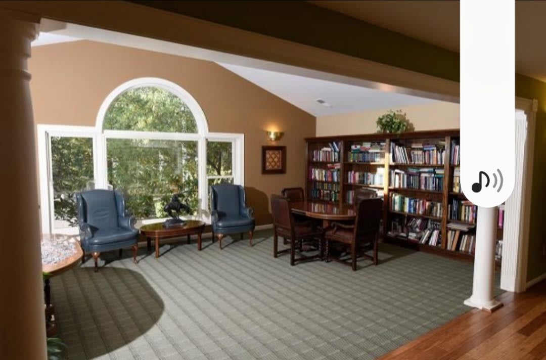Cozy library with wooden bookshelves and armchairs by a large window.