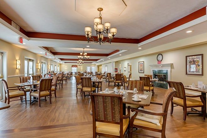 A spacious dining room with neatly arranged tables and chairs, illuminated by elegant chandeliers.