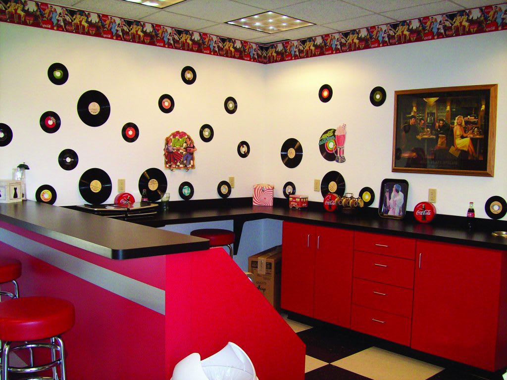 A retro-themed diner interior with vinyl records decorating the walls, red cabinetry, and a black and white checkered floor.