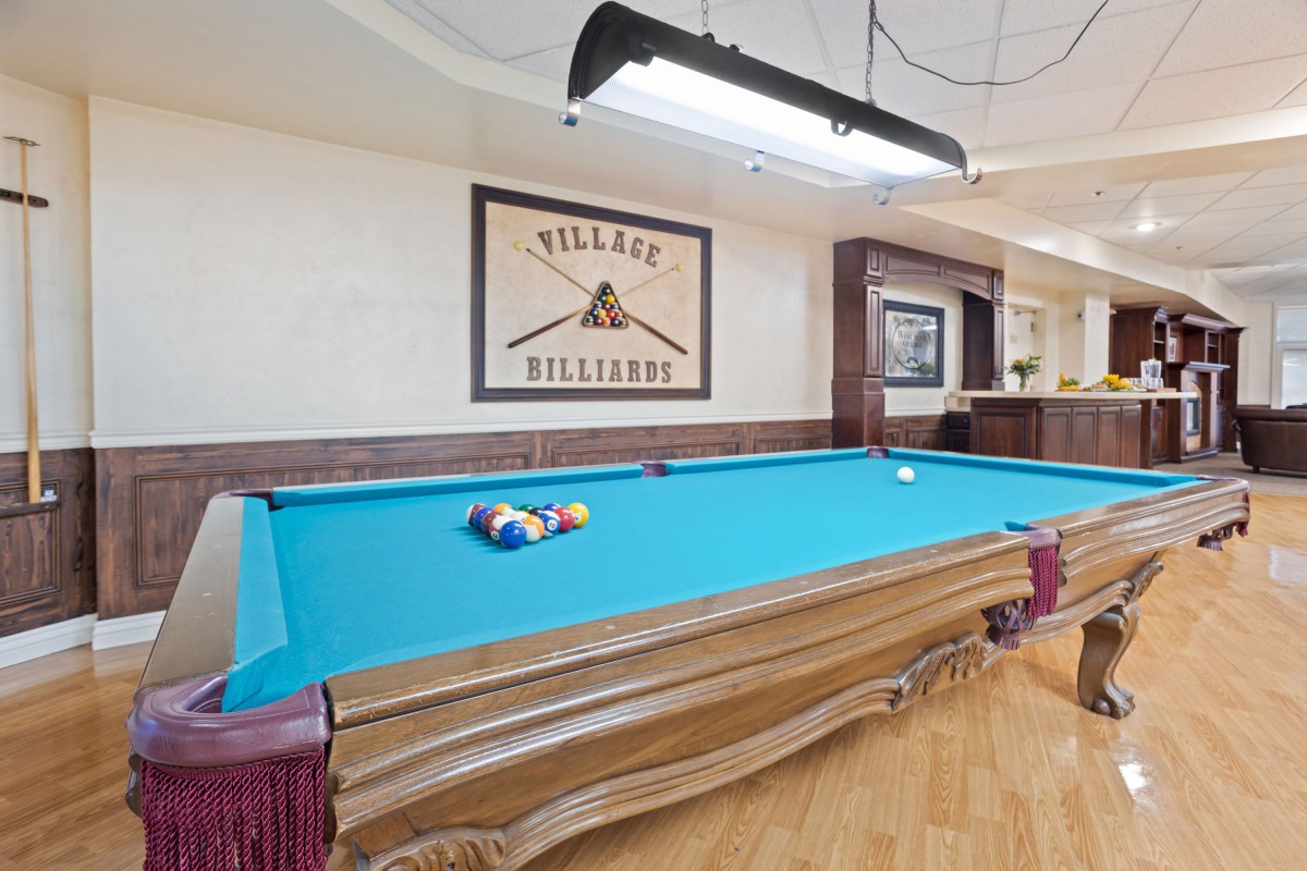 A stylish billiards room featuring a classic pool table with vibrant cloth, surrounded by vintage decor and wood flooring.