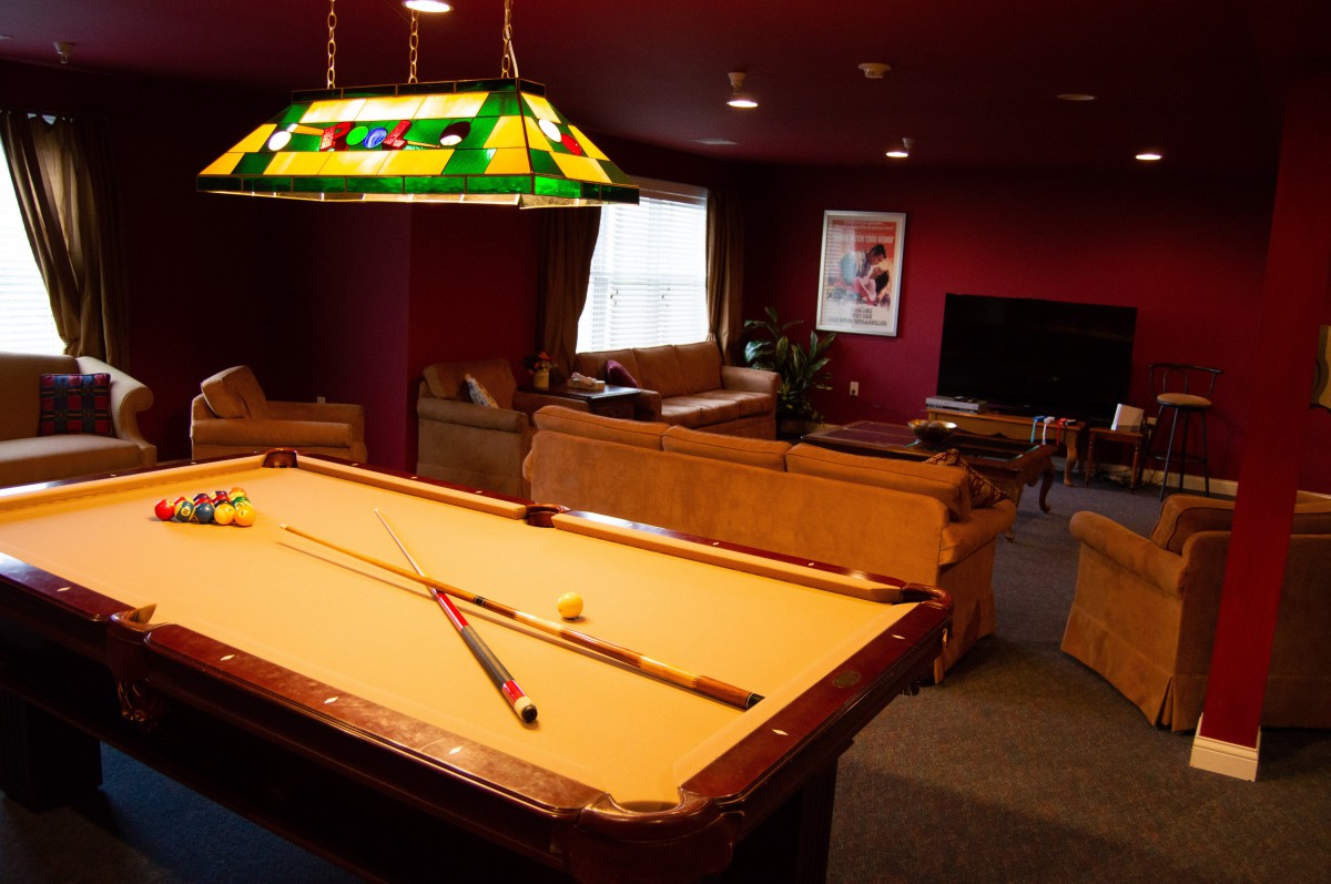 A cozy game room featuring a pool table illuminated by a stained glass lamp, with comfortable sofas and a television in the background.
