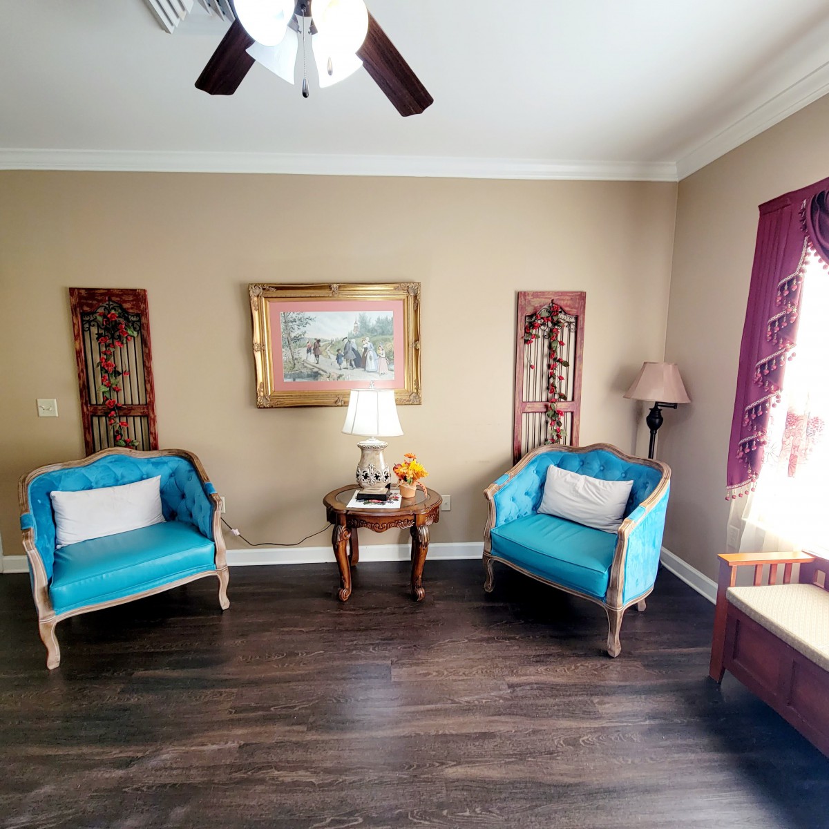 A cozy living room with teal chairs, a lamp on a side table, and artwork on the walls.