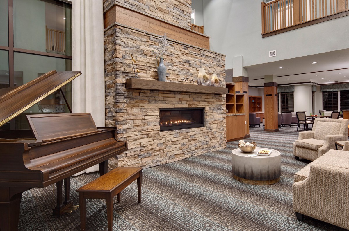 A modern living room featuring a stone fireplace and a piano.