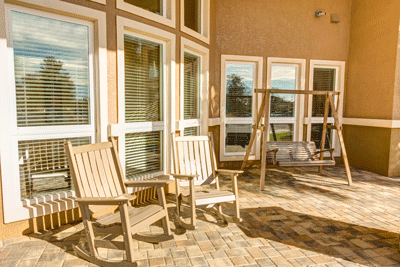 A sunny patio with rocking chairs and a swing, surrounded by large windows.
