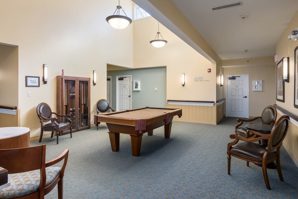 A spacious game room featuring a pool table and seating area with elegant lighting.