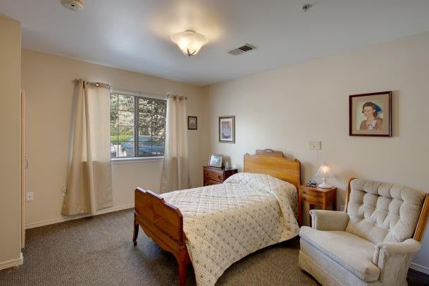A cozy bedroom with a single bed, chair, and natural light from the window.