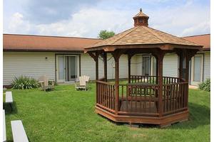 A wooden gazebo sits on a grassy lawn near a house.
