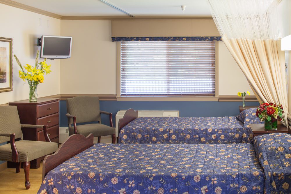 A hospital room with two beds, a television, and a window.