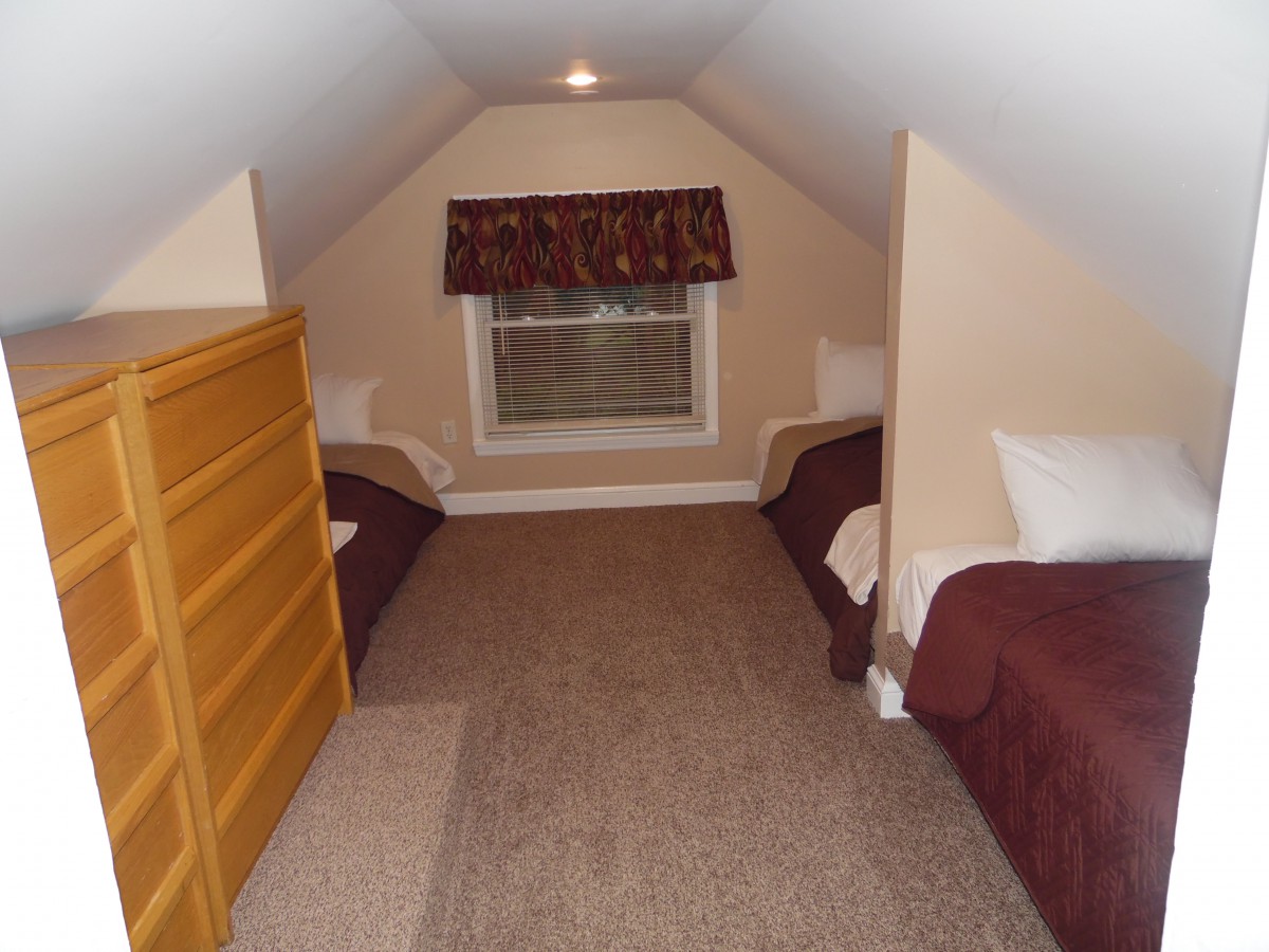 A small attic bedroom with two twin beds and a window with drapes.