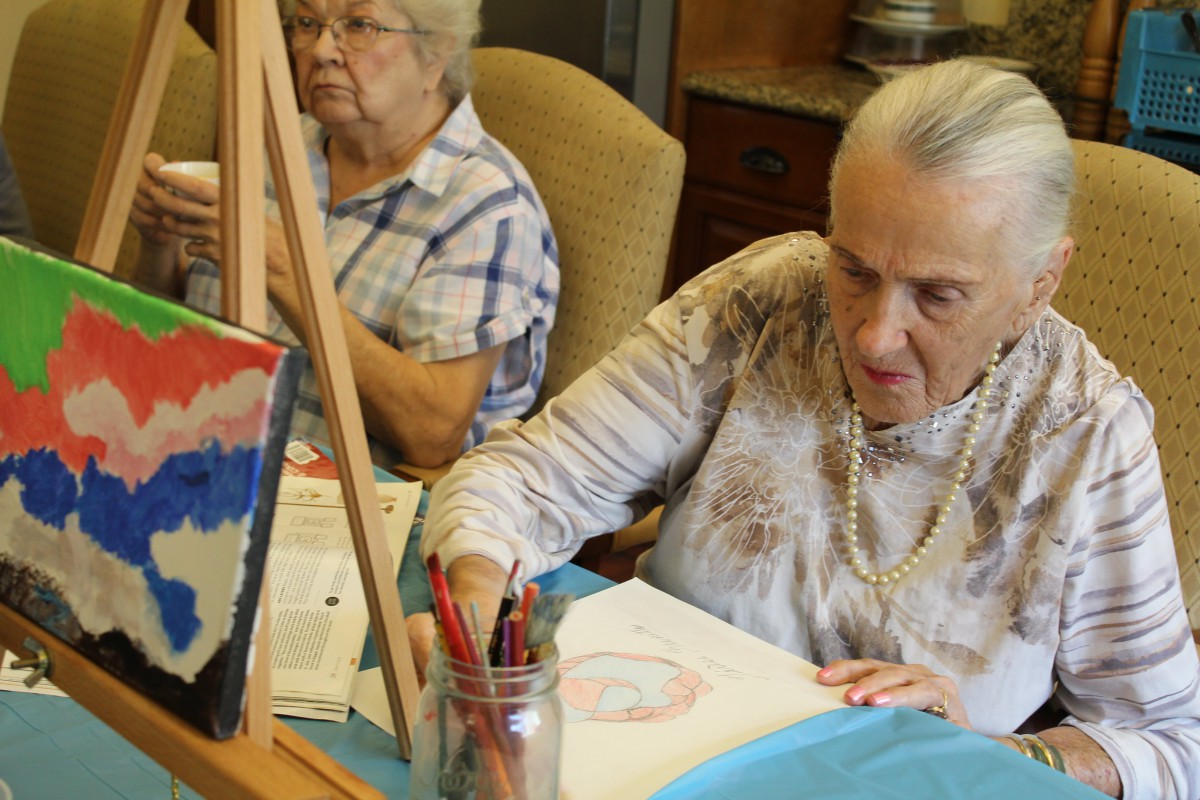 Two elderly women engaging in a painting activity indoors.