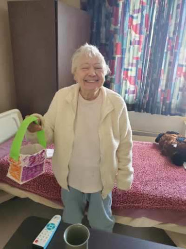 A cheerful elderly woman holding a colorful tote bag in her room.
