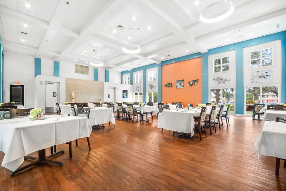 A spacious restaurant dining area with neatly arranged tables and chairs, featuring bright lighting and a wooden floor.