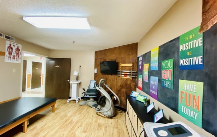 A modern chiropractic clinic treatment room with various therapy equipment and motivational posters on the walls.