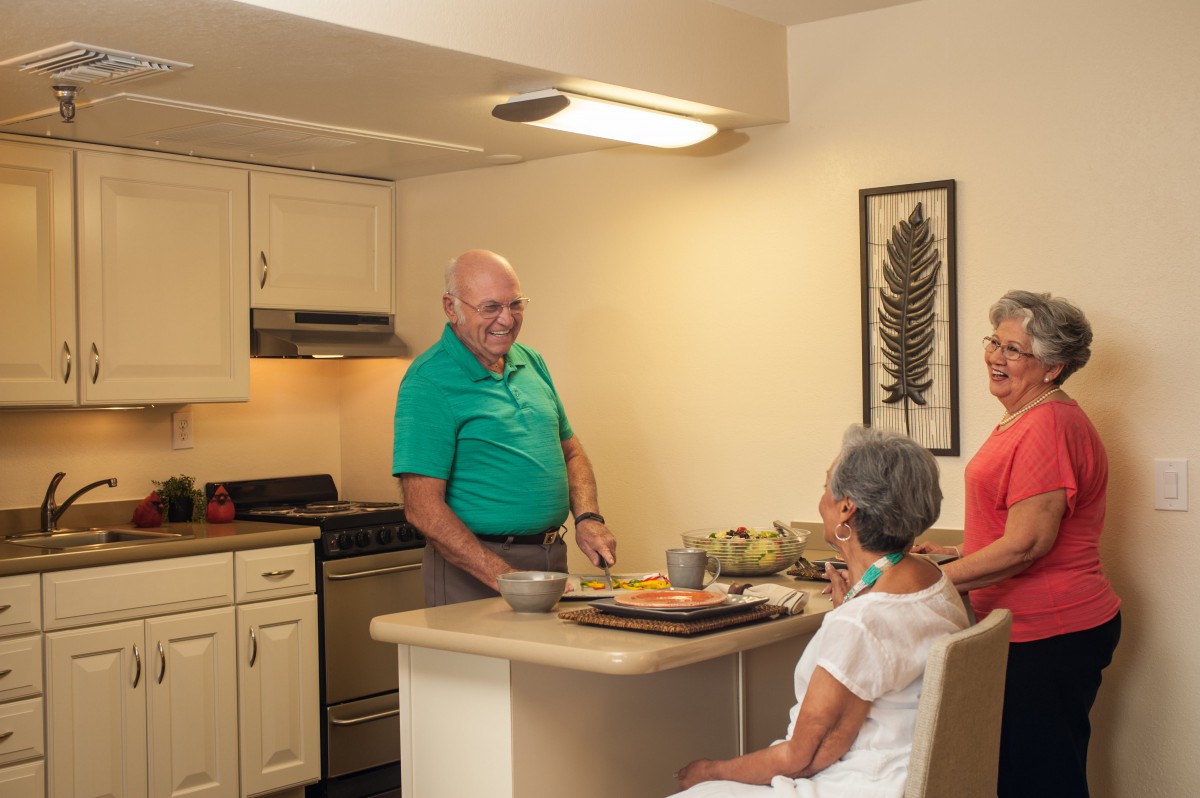 A family enjoys a conversation in the kitchen while preparing a meal.