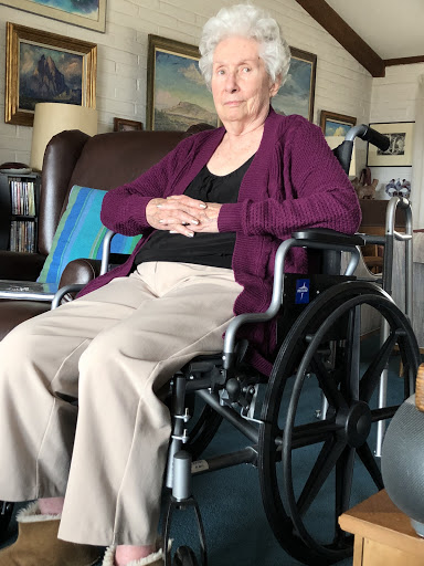 An elderly woman sitting in a wheelchair, looking thoughtfully ahead.