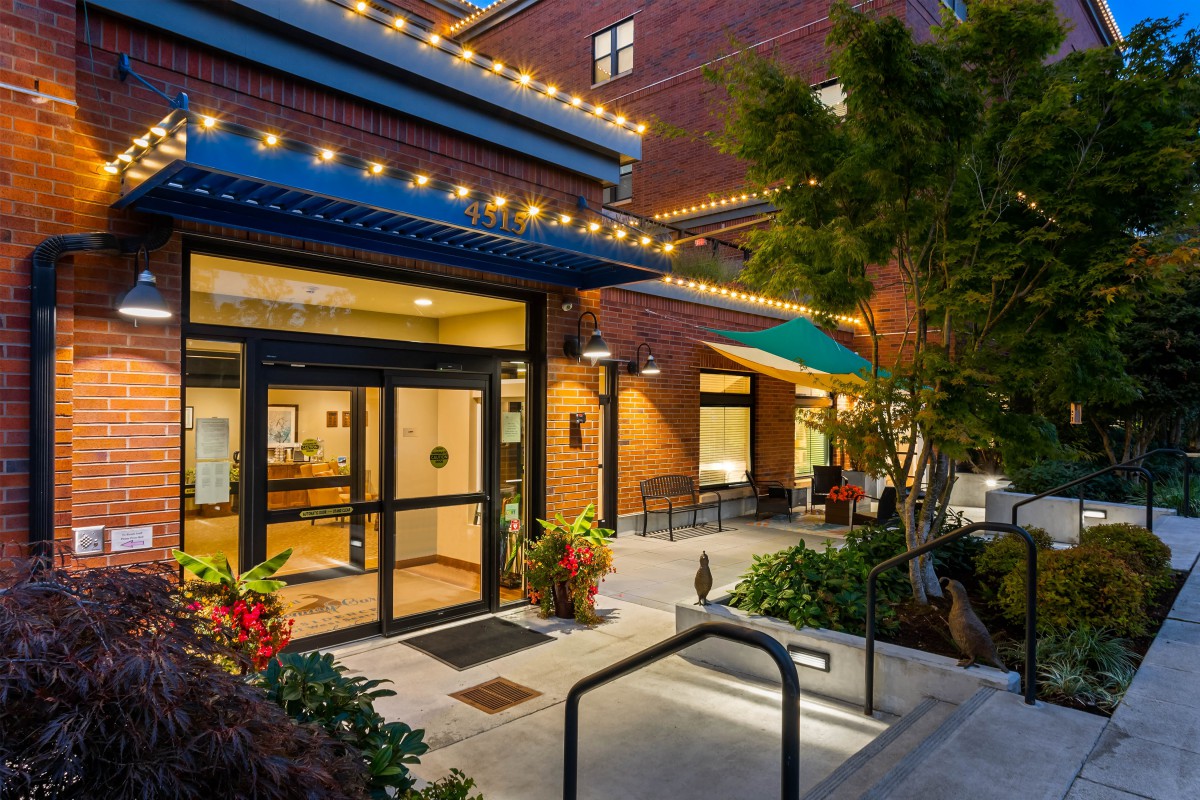 A well-lit building entrance with outdoor seating and decorative plants at night.