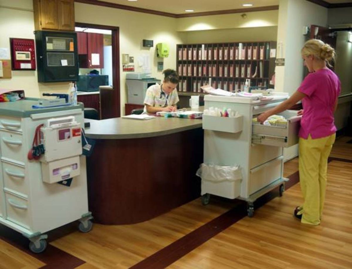 A nurse at a hospital reception desk with medical equipment in the foreground.