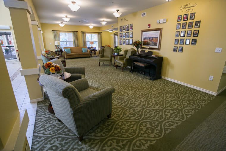 A cozy living room with comfortable seating and a piano, well-lit and decorated with photos on the walls.