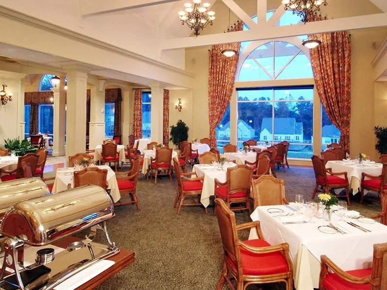 Elegant dining area with neatly arranged tables and chairs, adorned with chandeliers and large windows with curtains.