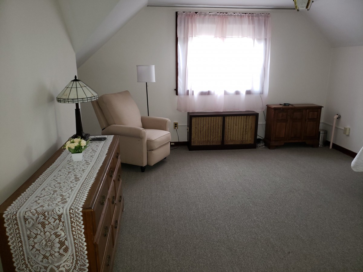 A cozy attic room featuring an armchair, a dresser, and a window with sheer curtains.
