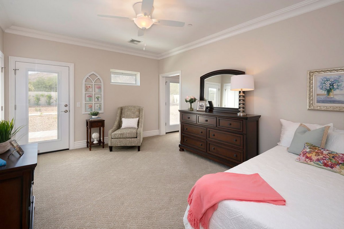A spacious and elegantly decorated bedroom featuring a large dresser with a mirror, an armchair, and soft lighting.