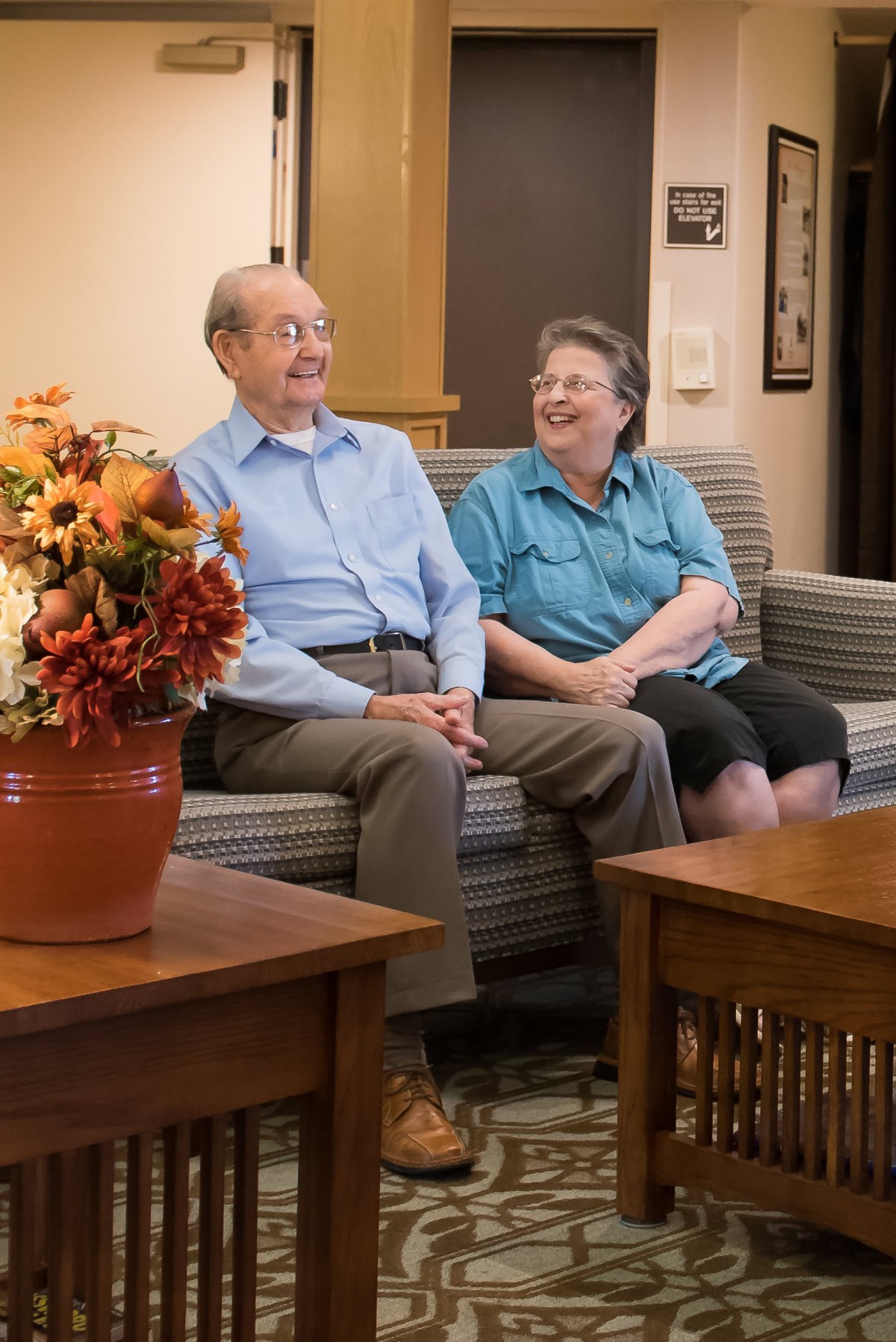 An elderly couple sitting and laughing together in a cozy living room.