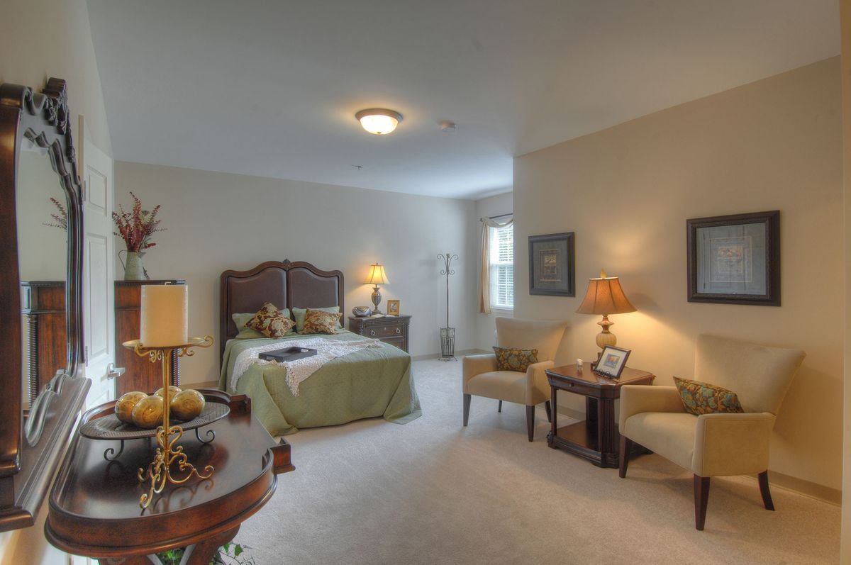A cozy and elegantly furnished bedroom featuring a large bed, chairs, and warm lighting.