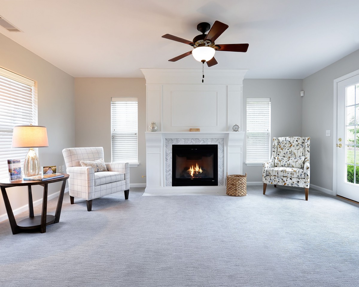 A cozy living room with a fireplace, armchairs, and ceiling fan.