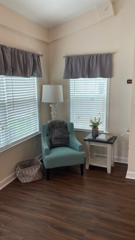 A cozy corner with a teal chair, white lamp, and side table by the window.